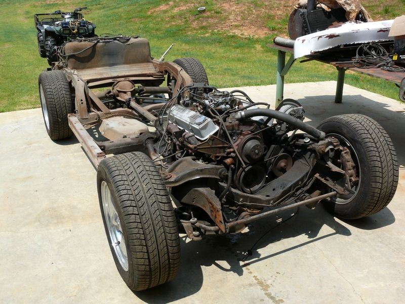 1976 Chevrolet Corvette chassis with engine and wheels, front view. ATV in background