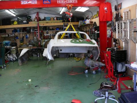 1976 Chevrolet Corvette - The rear section of a car is suspended in a workshop, undergoing repairs or restoration.