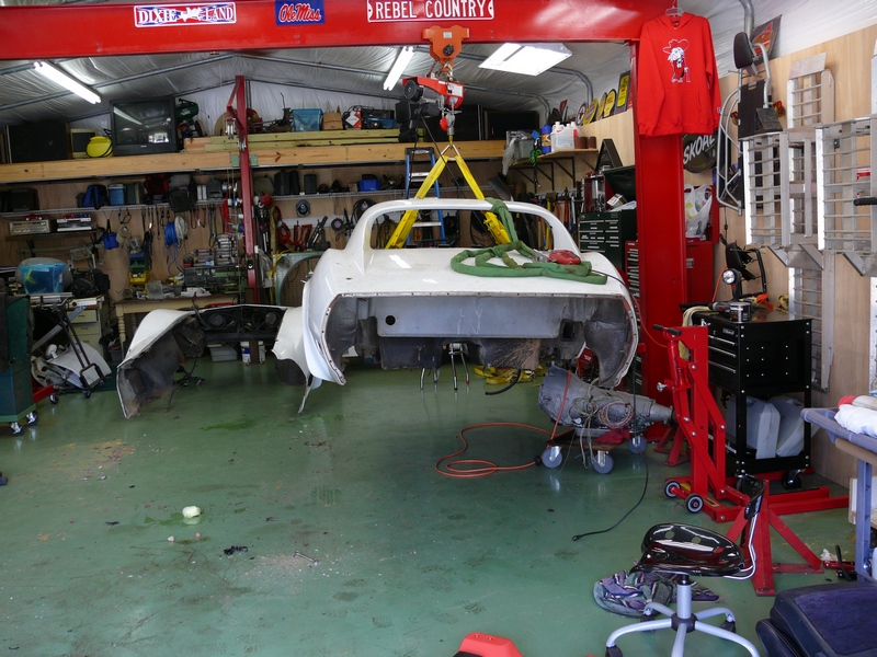 Car body lifted by a crane in a garage with tools and parts around