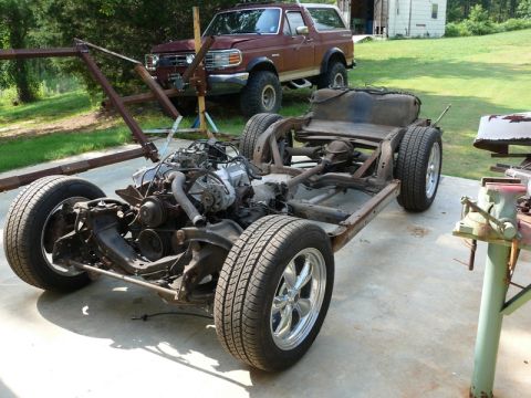 1976 Chevrolet Corvette - A car's chassis and engine are displayed outdoors, with a maroon SUV parked behind it.