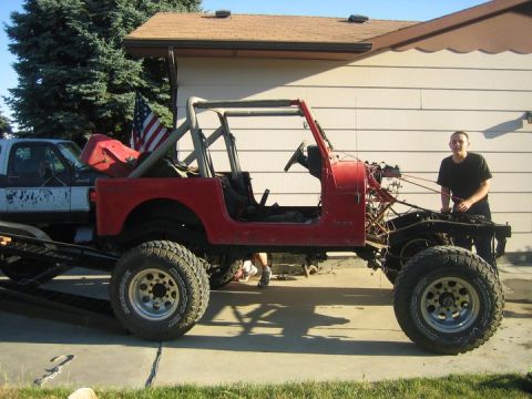 1990 Jeep YJ - A man stands by a red Jeep CJ, which is being loaded onto a trailer by a pickup truck.