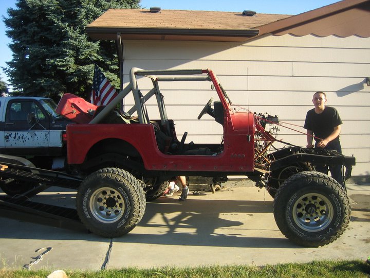 Red Jeep CJ being loaded onto a trailer next to a pickup truck