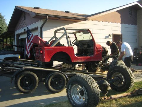 1990 Jeep YJ - A red Jeep CJ-7 body is loaded onto a trailer, with two men attending to it in front of a house.