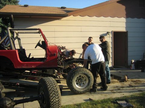 1990 Jeep YJ - Four people are gathered around the frame of a red Jeep YJ, appearing to be working on it.