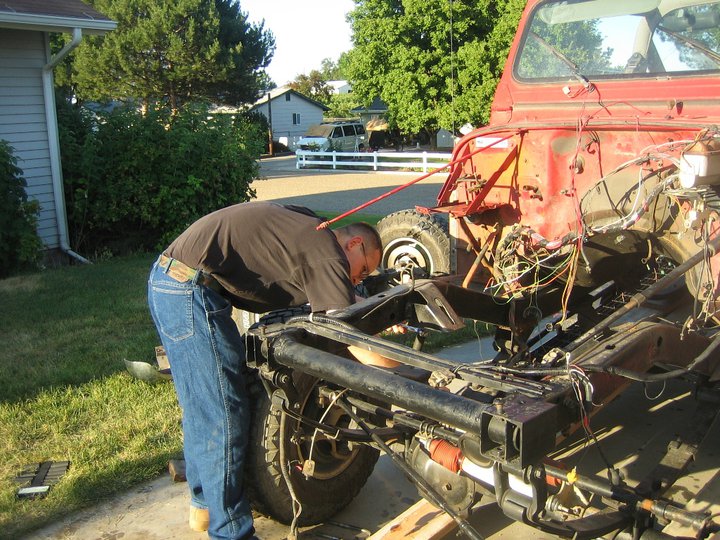 Man in jeans and black shirt bends over to work on the chassis of a red Jeep YJ, with wiring exposed