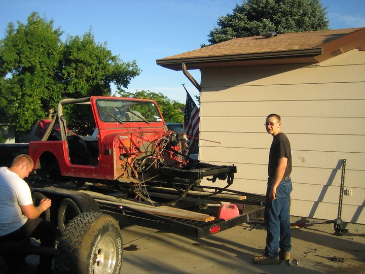 Red Jeep CJ-7 on trailer, engine removed, with two guys nearby