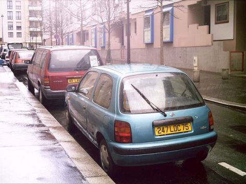 1991 Ford LTD Crown Victoria - A blue Nissan Micra is parked on a wet street next to a red minivan.