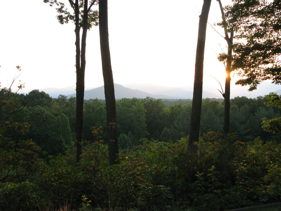 Trees in foreground with mountains and forest in background at sunset. Supermotors.net logo visible