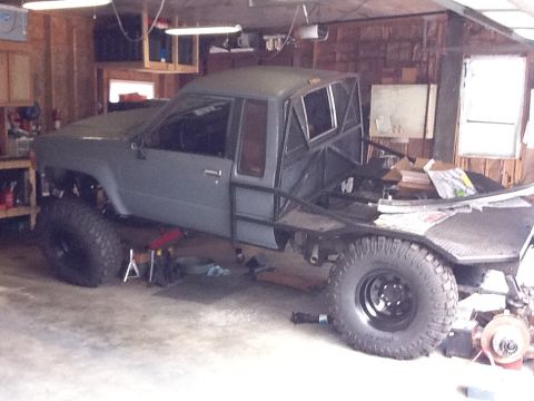 1988 Suzuki Samurai - This modified pickup truck features an extended cab, flatbed, and a custom roll cage, sitting high on off-road tires.