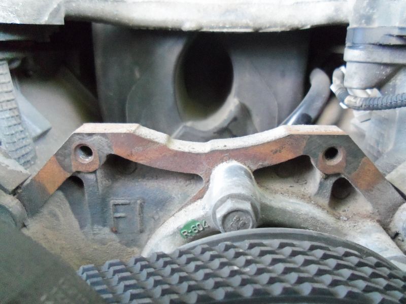 Close-up of an engine component with a ribbed belt visible below. Part number R-604 is stamped on the metal
