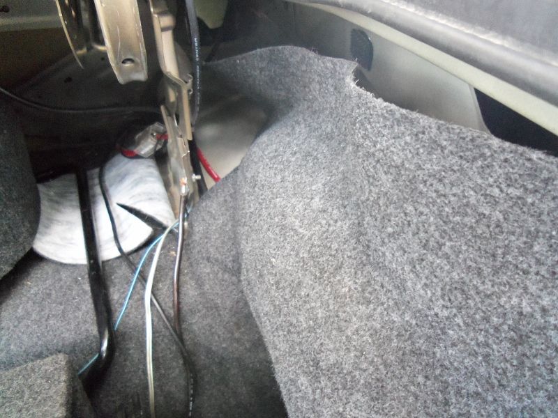 Car trunk interior with gray carpet lining, exposed wiring, and metal brackets