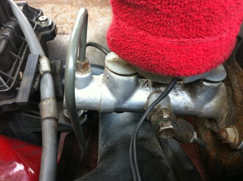 1990 Mazda Miata - Close-up view of a brake master cylinder, partially covered by a red fabric material.