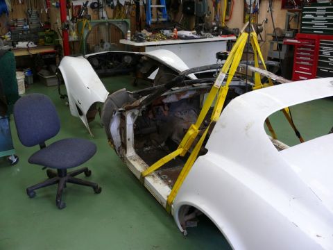 1976 Chevrolet Corvette - A car body is suspended by a yellow lift in a cluttered workshop, undergoing repairs.