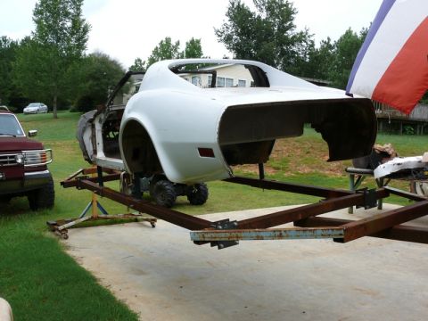 1976 Chevrolet Corvette - The rear section of a white Corvette body is elevated on a trailer, with a red pickup truck parked nearby.
