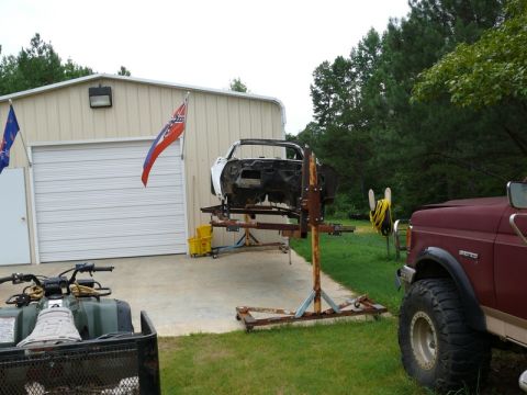 1976 Chevrolet Corvette - The body of a 1976 Chevrolet Corvette is elevated on a stand in front of a garage, with an ATV and a truck nearby.