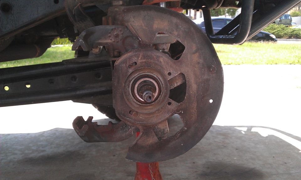 Rusted brake rotor and hub assembly on a vehicle's suspension, supported by a red jack stand