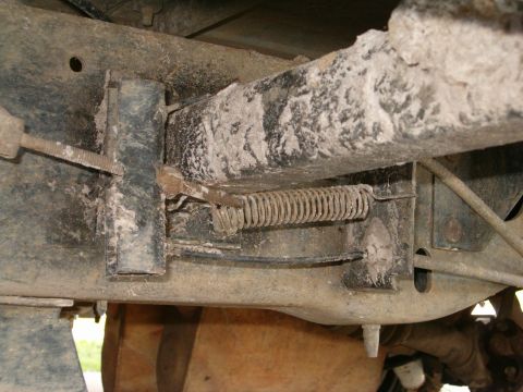 1991 Ford Bronco - Close-up underbody shot of a dirt- and mud-caked truck frame rail showing a coil return spring anchored between a bracket and a lever arm,…