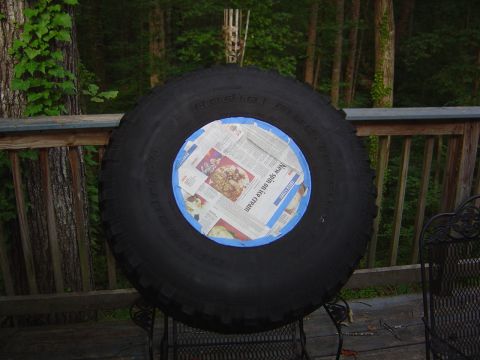 1986 Ford Bronco - A tire is covered with newspaper and blue tape, resting on a table outdoors.