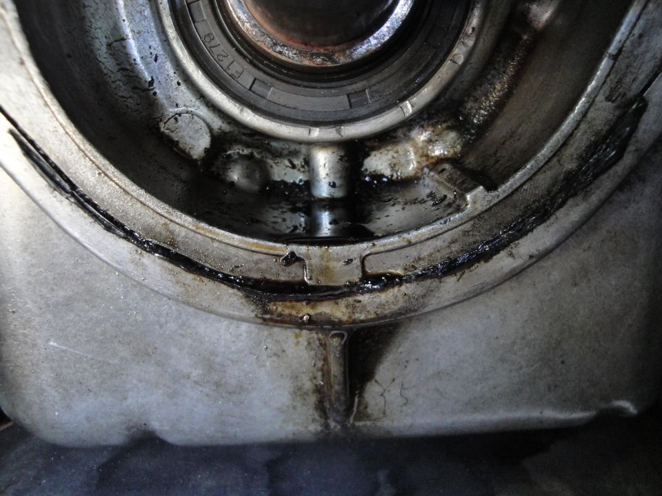 Close-up of a greasy engine part, possibly a seal or bearing housing, showing signs of an oil leak