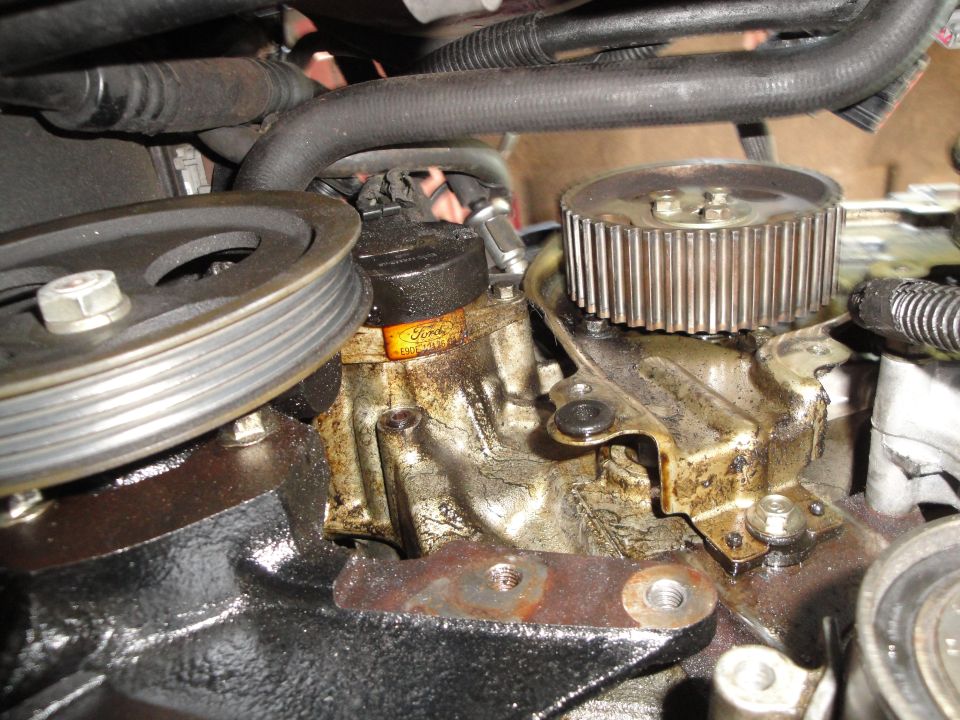 Close-up of engine parts, including a pulley and a toothed wheel. A label with 'Ford' is visible