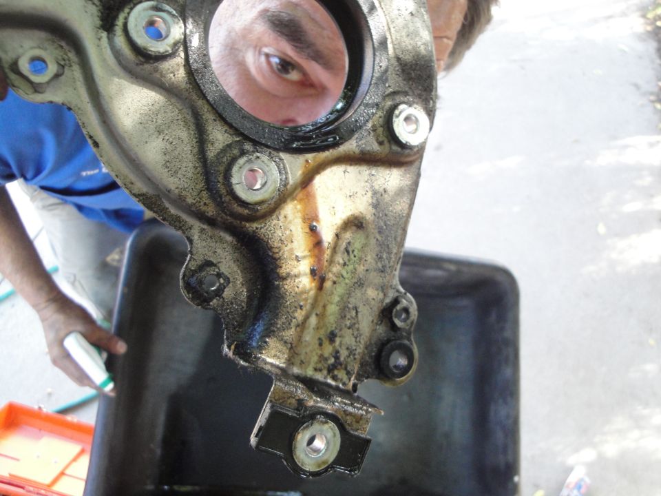 Greasy metal car part with bolts and a man's eye reflected in a circular opening