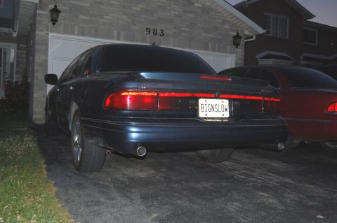 1985 Mercury Grand Marquis - A dark blue sedan is parked in a driveway at night, with another red car partially visible to its right.