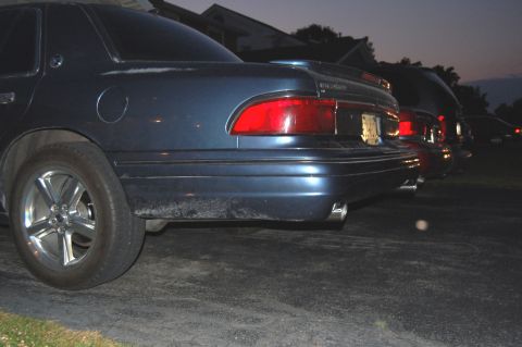 1985 Mercury Grand Marquis - Rear view of a dark blue sedan parked in a line of vehicles as dusk settles.