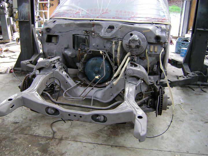 Front end of stripped car body on lift showing brake booster, subframe and rotors