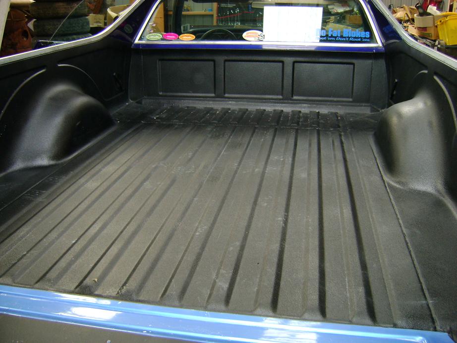 Black bed liner in the cargo bed of a blue Ford Ranchero, viewed from the rear in a garage