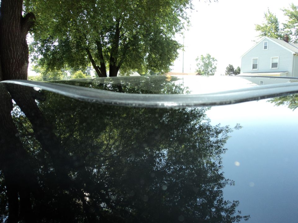 Black car roof edge with reflection of trees and a house
