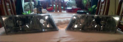 2001 Mercury Grand Marquis - Two car headlights are displayed on a table, possibly before or after restoration.