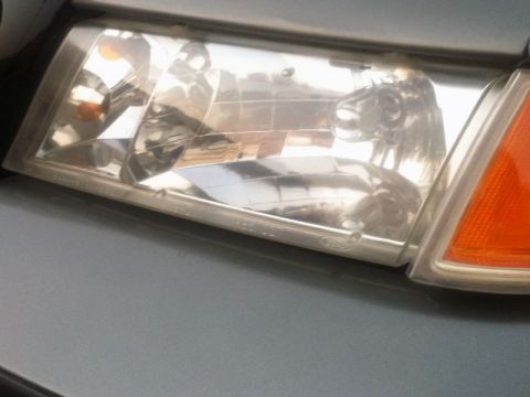 2001 Mercury Grand Marquis - Close-up of a 2001 Mercury Grand Marquis headlight assembly on a gray vehicle.