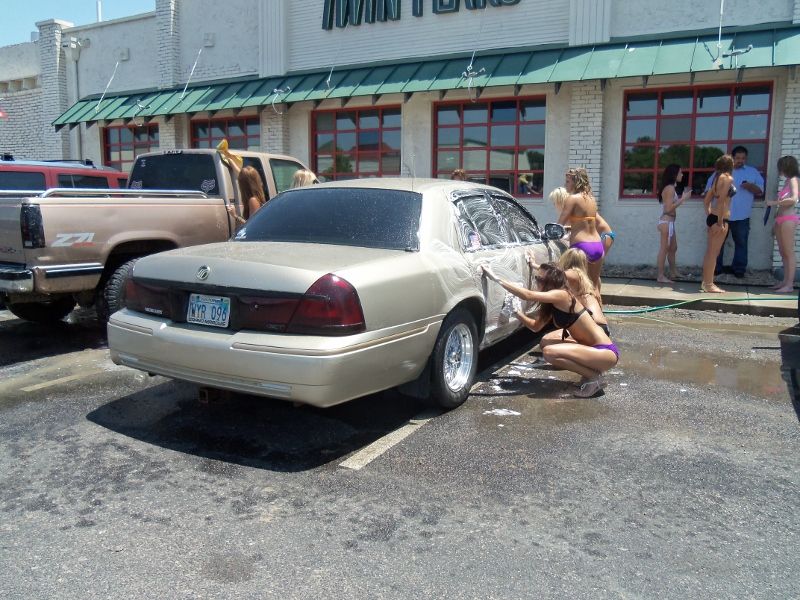Gold 2000 Mercury Grand Marquis sedan, rear 3/4 view, being washed by women