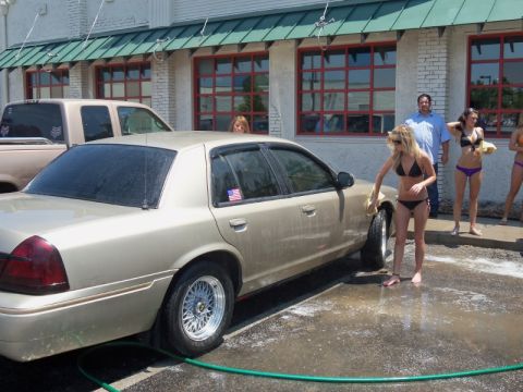 2000 Mercury Grand Marquis - A gold 2000 Mercury Grand Marquis is being washed by women in bikinis at a car wash, with another vehicle visible in the background.