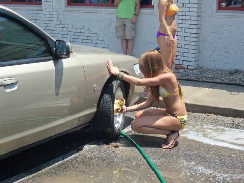 2000 Mercury Grand Marquis - A woman washes the wheel of a car while two other people stand nearby.