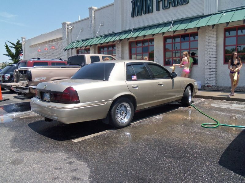 Gold sedan parked at a car wash, side view. Water on the ground
