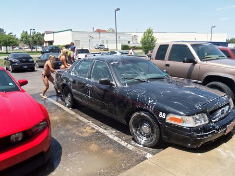 2000 Mercury Grand Marquis - People in bikinis wash a black sedan at a carwash, with other vehicles nearby.