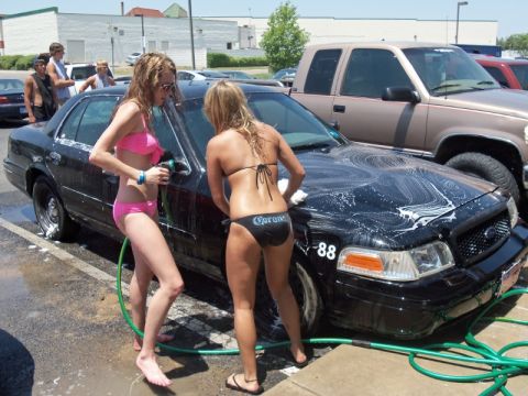 2000 Mercury Grand Marquis - Two women in bikinis wash a black sedan at a car wash, with a pickup truck visible in the background.