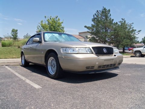 2000 Mercury Grand Marquis - Gold 2000 Mercury Grand Marquis parked in a lot under a blue sky.