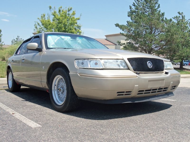 Gold 2000 Mercury Grand Marquis parked outside with trees and buildings in the background