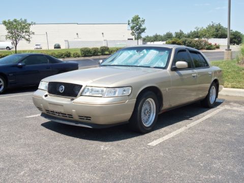 2000 Mercury Grand Marquis - A gold 2000 Mercury Grand Marquis is parked in a lot next to a dark-colored car.