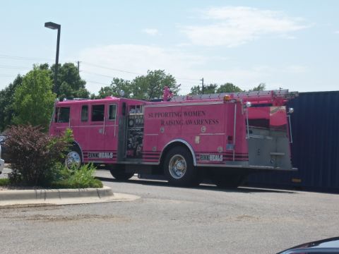 2000 Mercury Grand Marquis - A pink fire truck is parked next to a dark blue container, with text on its side indicating support for breast cancer awareness.