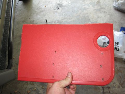 2005 Jeep Wrangler - A red dashboard component, possibly a cover or panel, is held up, showing a silver circular emblem.