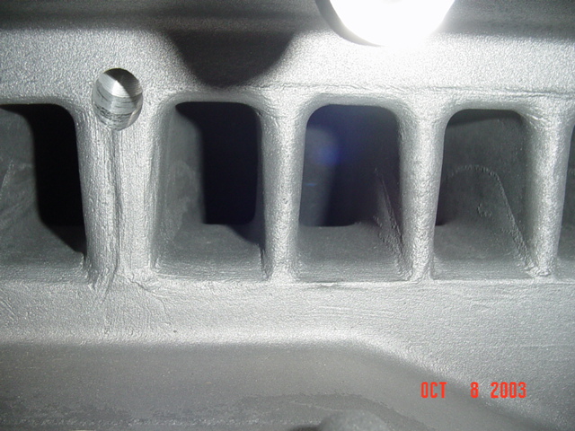 Close-up of cast aluminum part with ribbed webbing and one threaded hole, lit by work light, dated Oct 2003