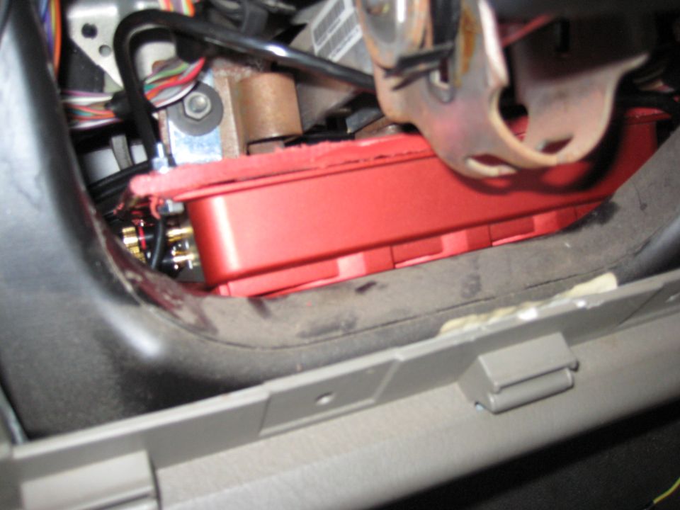 Red amplifier mounted under dash near steering column and pedal linkage with RCA inputs visible