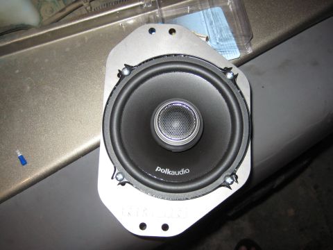 2005 Jeep Wrangler - A Polk Audio coaxial car speaker bolted to a gray metal/plastic adapter mounting bracket, resting on a khaki-painted body panel with the cl…