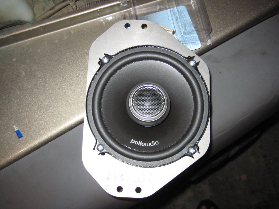 Polk Audio coaxial speaker mounted on gray adapter bracket sitting on olive body panel