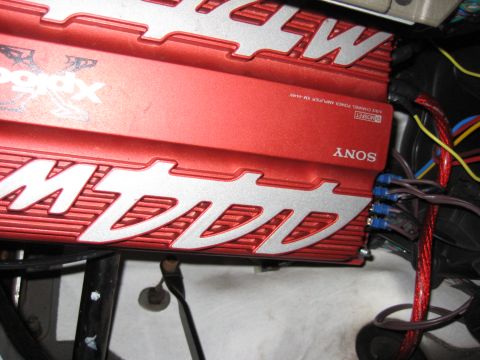 2005 Jeep Wrangler - Tight shot of a red Sony Xplod XM-444W four-channel MOSFET power amplifier mounted upside down under a vehicle's dash, its silver-lettered…