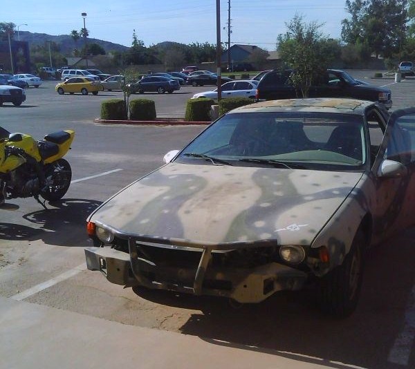 Car with camouflage paint, missing front bumper, and open driver's door