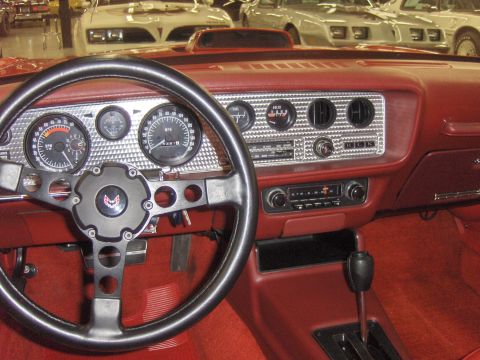 1979 Chevrolet Camaro - Interior view of a 1977 Pontiac Firebird, showing the dashboard, steering wheel, and shifter. Multiple vehicles are visible in the backgrou…